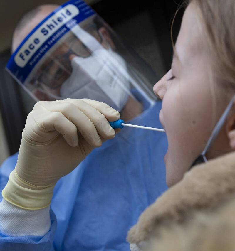 Doctor wearing protective clothing and using a medical mouth swab to test a teenager for Covid-19