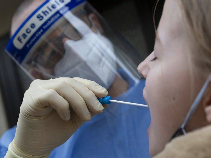 Doctor wearing protective clothing and using a medical mouth swab to test a teenager for Covid-19